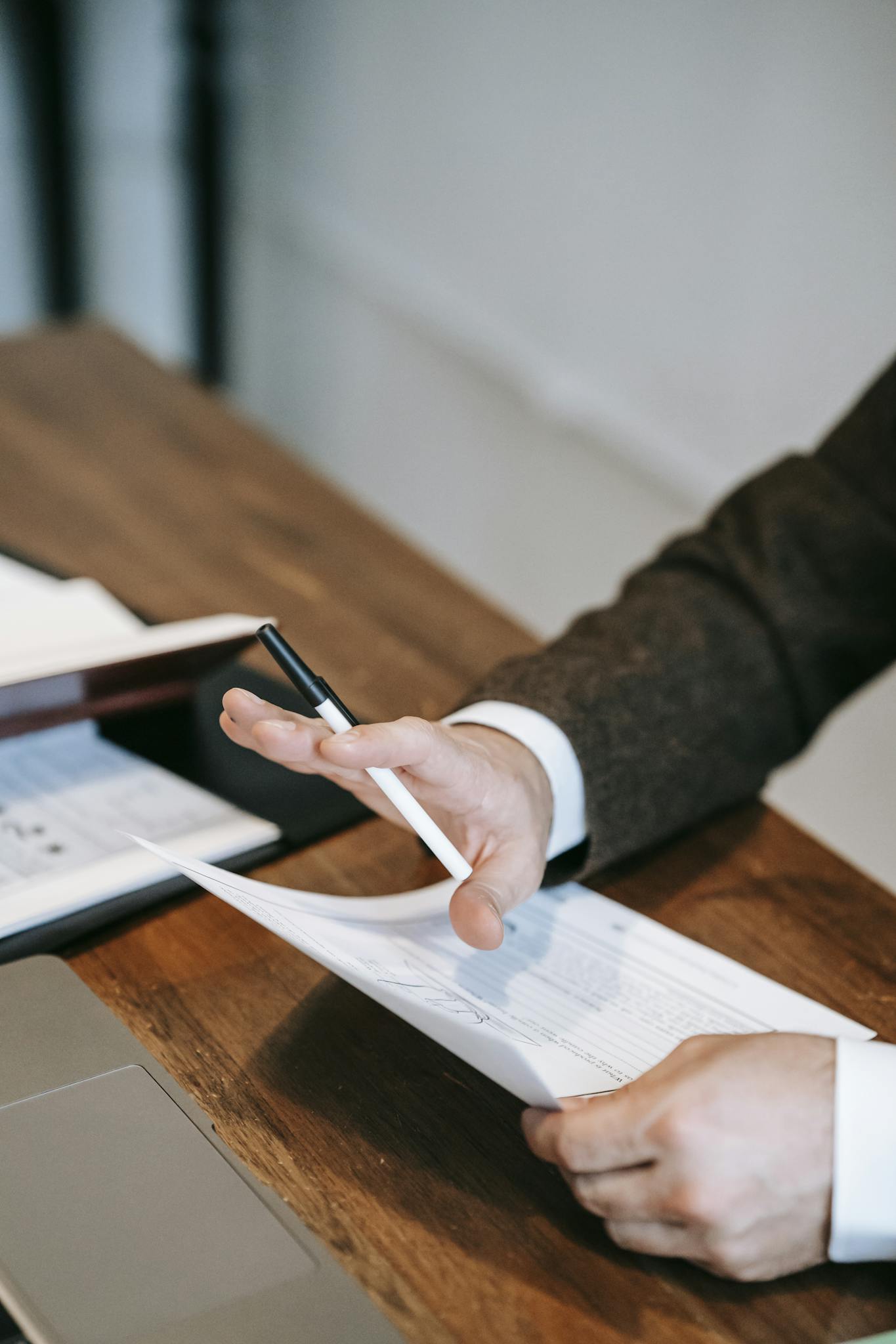 Close-up of a businessman in a suit analyzing papers on a wooden desk.