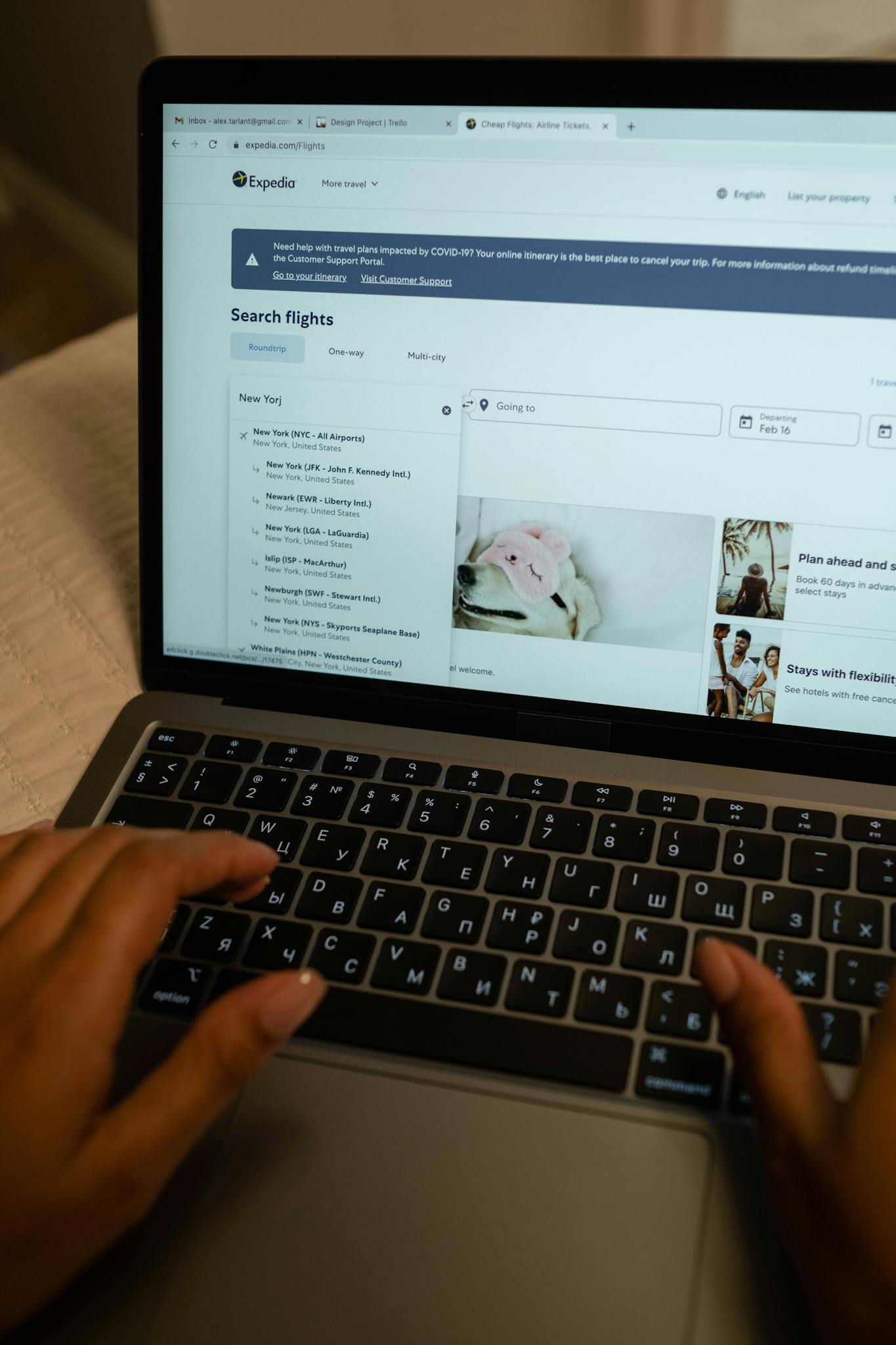 Person typing on laptop, searching flight details indoors, focusing on travel planning and booking.